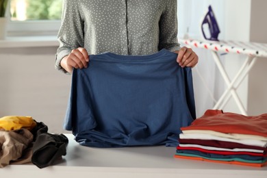 Woman folding clothes at white table indoors, closeup