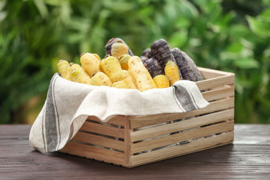 Photo of Different raw carrots in crate on wooden table against blurred background