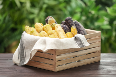 Different raw carrots in crate on wooden table against blurred background