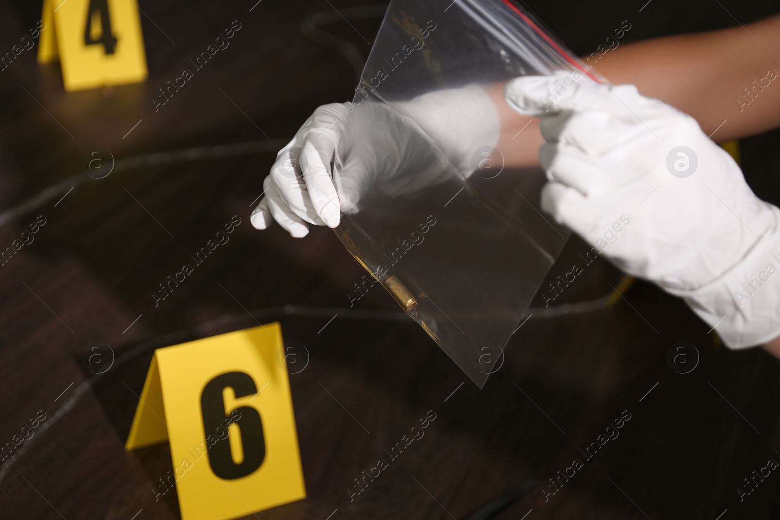 Photo of Detective holding plastic bag with bullet shell at crime scene, closeup