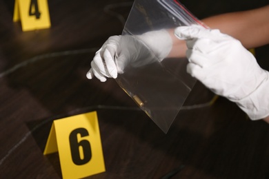 Photo of Detective holding plastic bag with bullet shell at crime scene, closeup