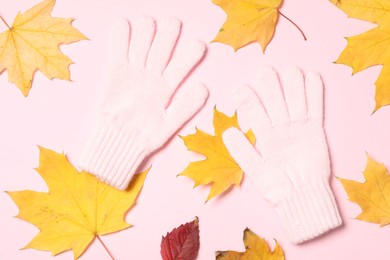 Stylish woolen gloves and dry leaves on pink background, flat lay