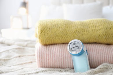 Modern fabric shaver and woolen sweaters on bed indoors, closeup