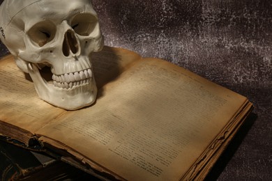 Photo of Human skull and old book on brown textured background, closeup