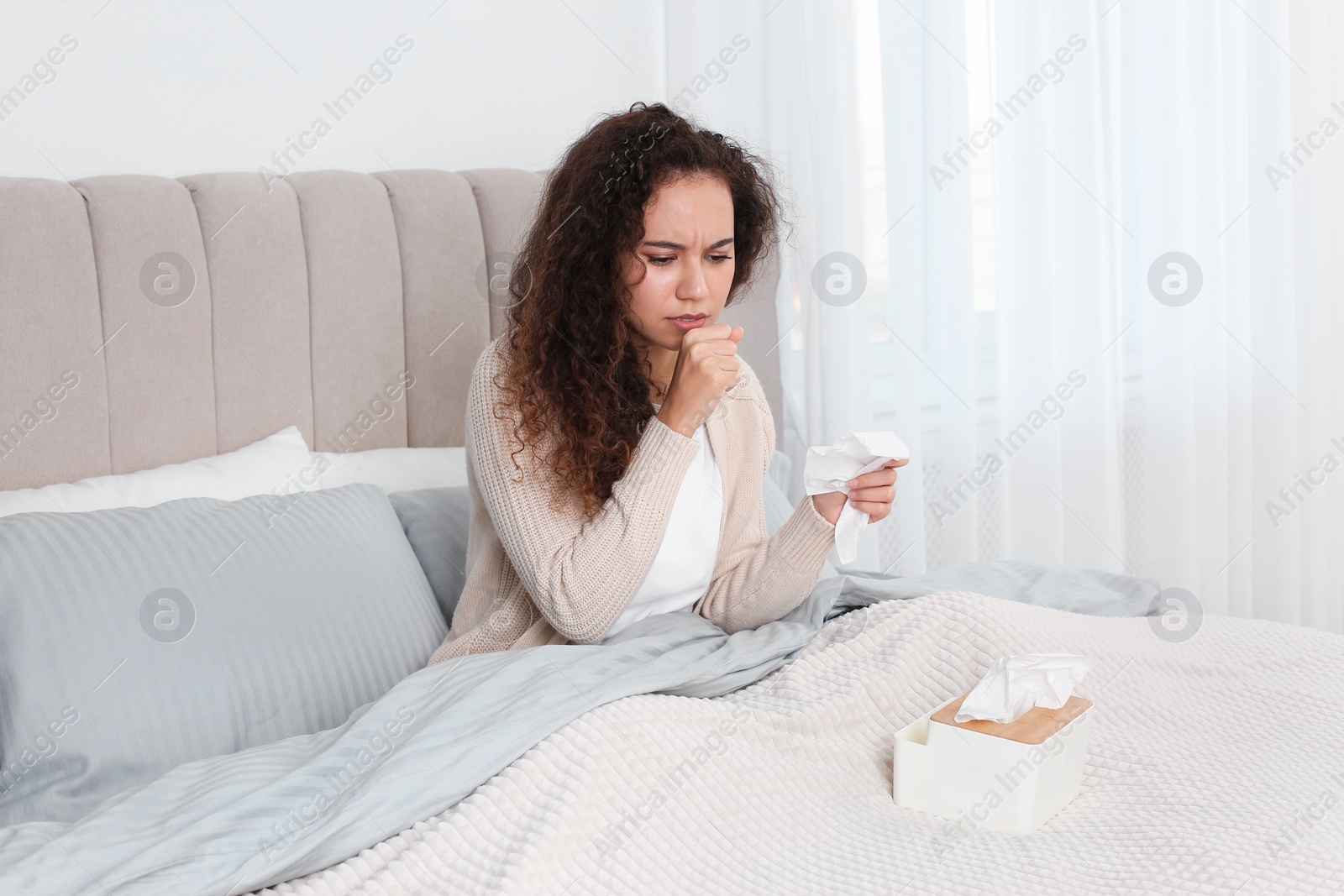 Photo of Sick African American woman with box of tissues in bed at home