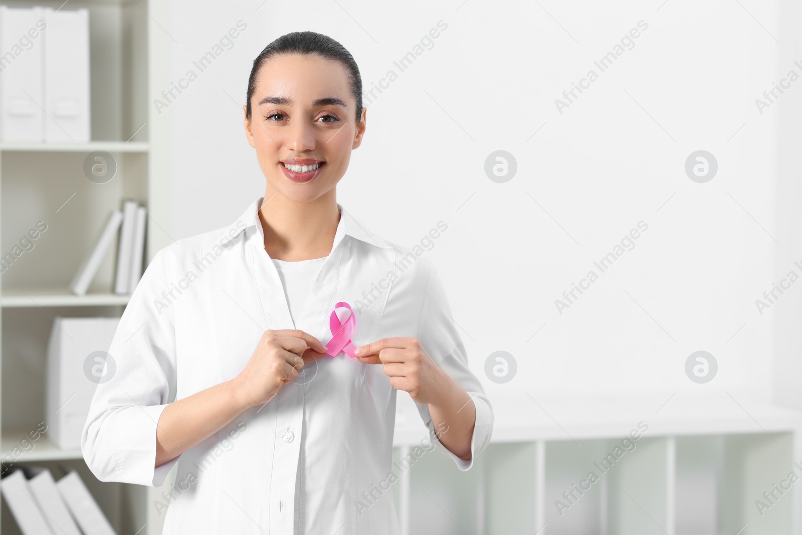 Photo of Mammologist with pink ribbon in hospital, space for text. Breast cancer awareness