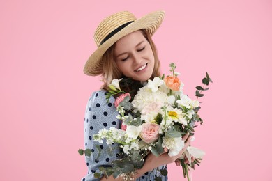 Beautiful woman in straw hat with bouquet of flowers on pink background