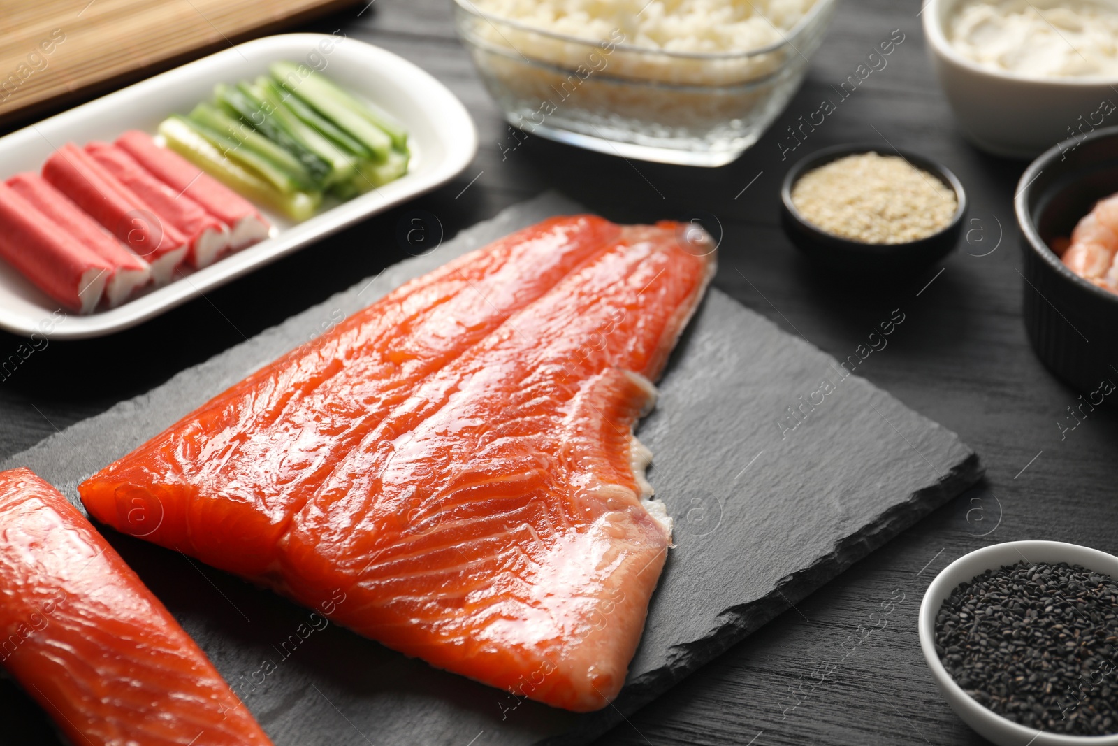 Photo of Making sushi rolls. Fresh salmon and other ingredients on black wooden table, closeup