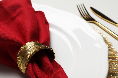 Plate with red fabric napkin, decorative ring and cutlery on white table, closeup