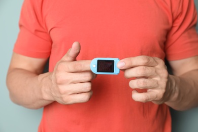 Photo of Young man checking pulse with blood pressure monitor on finger against color background, closeup