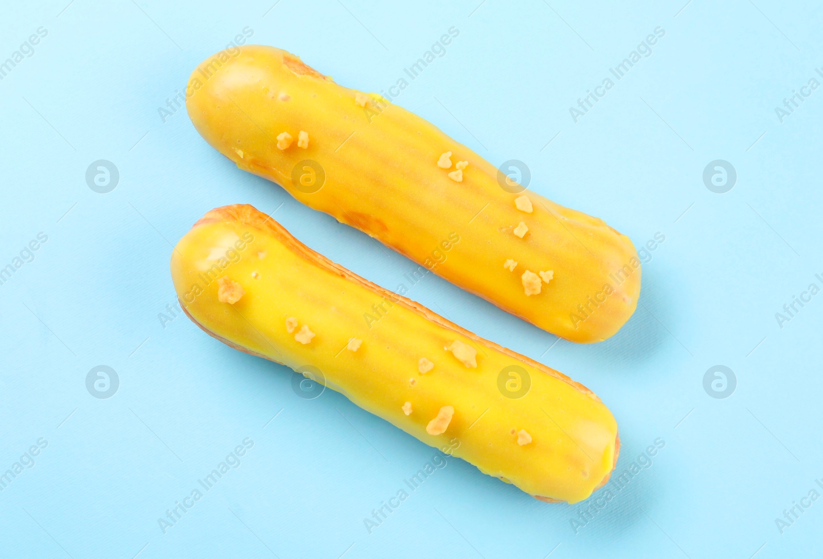 Photo of Delicious eclairs covered with glaze on light blue background, top view