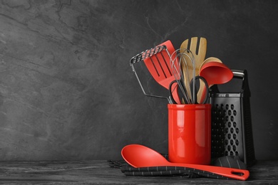 Photo of Holder with kitchen utensils on grey table against dark background. Space for text