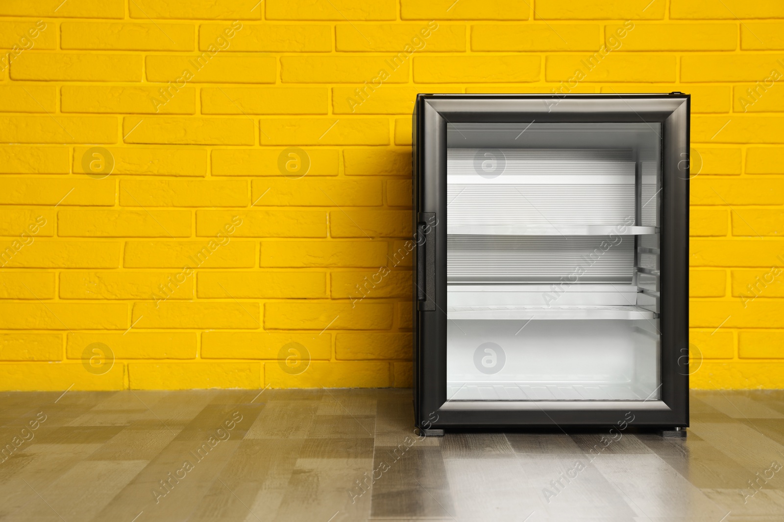 Photo of Empty mini bar with glass door near yellow brick wall, space for text