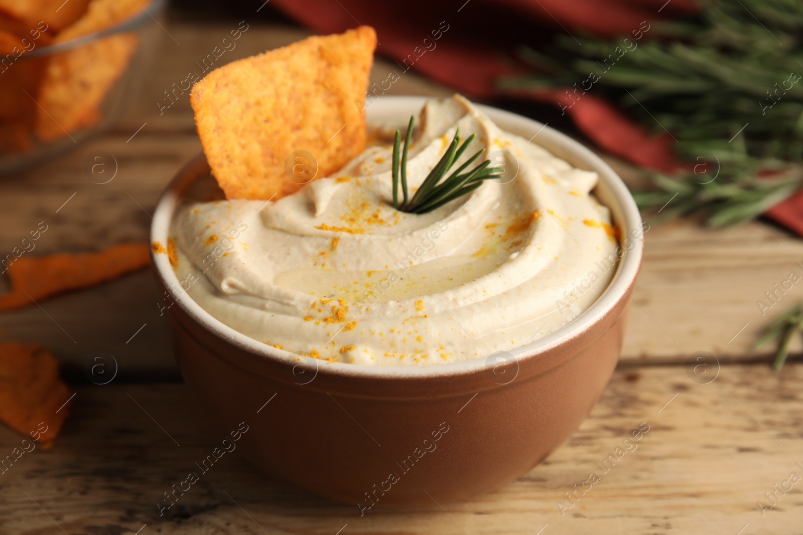 Photo of Delicious hummus with nachos and rosemary on wooden table, closeup