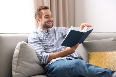 Photo of Handsome young man reading book on sofa at home