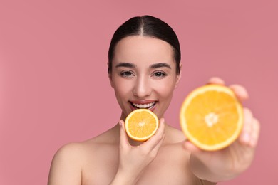 Photo of Beautiful young woman with pieces of orange on pink background, selective focus