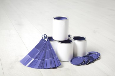 Image of Cans of violet paints and color palette samples on wooden floor indoors