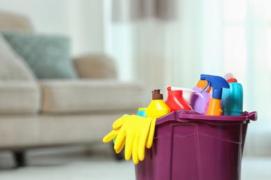 Photo of Plastic bucket with different cleaning products indoors, space for text