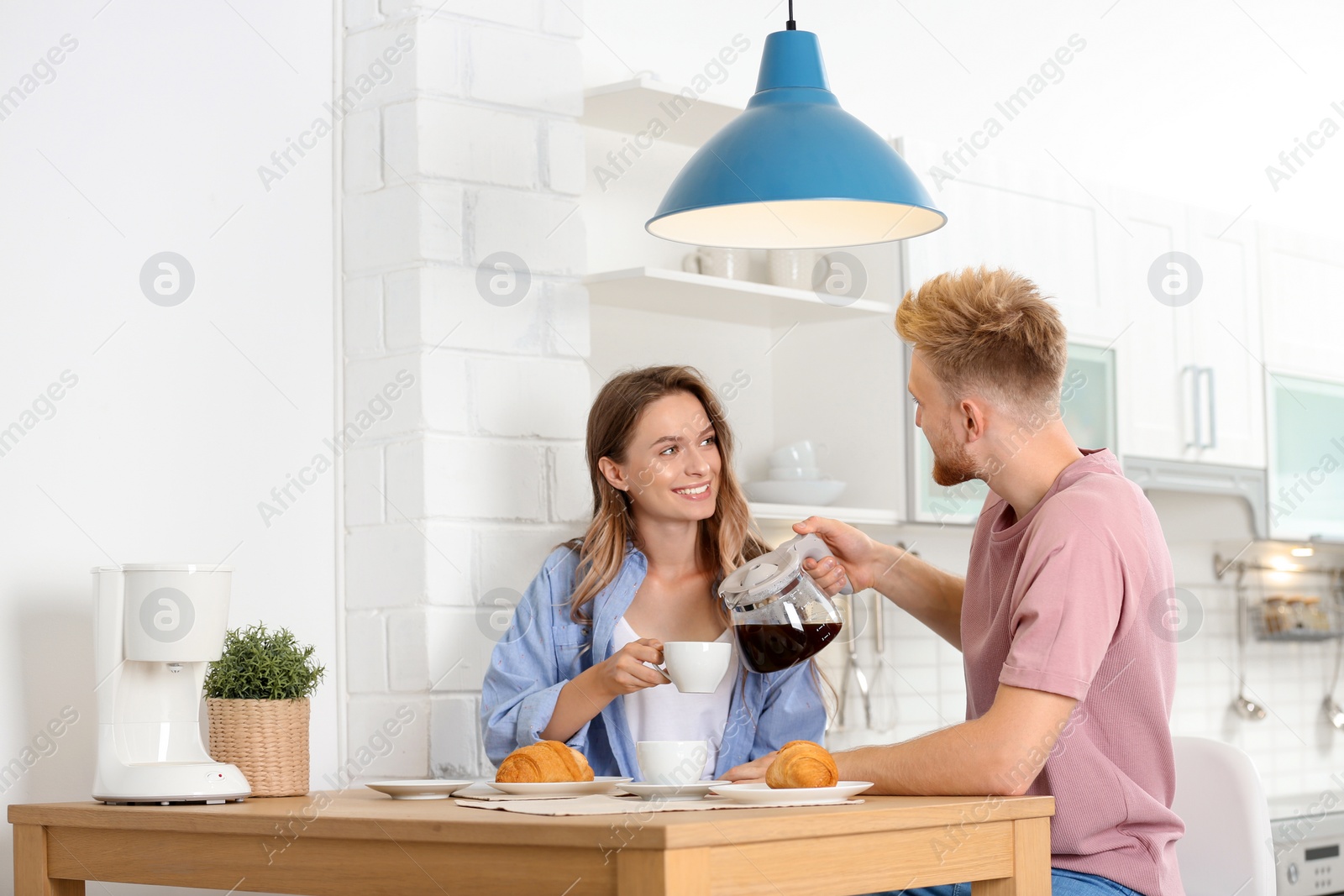 Photo of Happy young couple having breakfast at table in kitchen