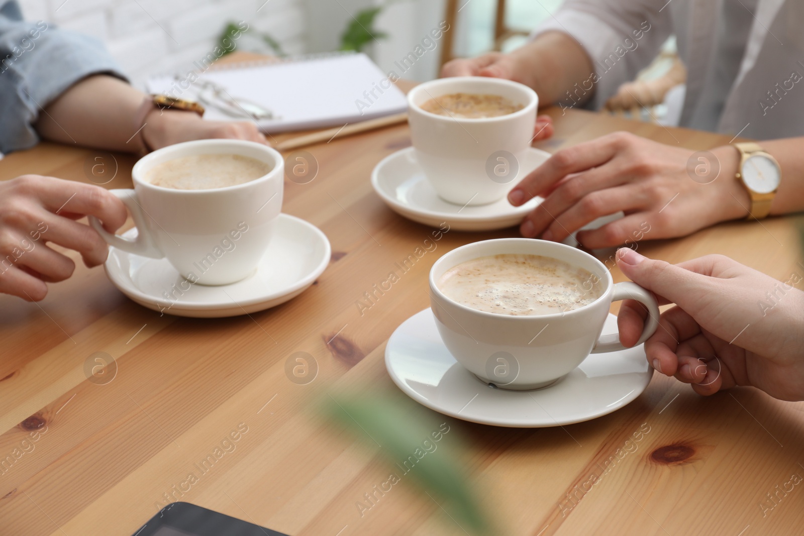 Photo of Women with cups of coffee at table in cafe, closeup