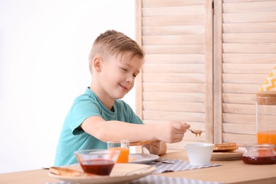 Photo of Cute little boy spreading jam onto tasty toasted bread at table