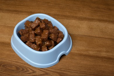 Wet pet food in feeding bowl on wooden background, space for text