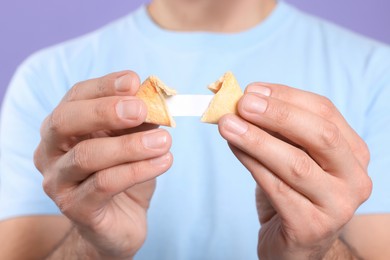 Man holding tasty fortune cookie with prediction on violet background, closeup