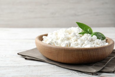 Delicious cottage cheese with basil in bowl on white wooden table, space for text