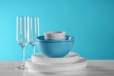 Photo of Set of clean dishes and glasses on table against color background