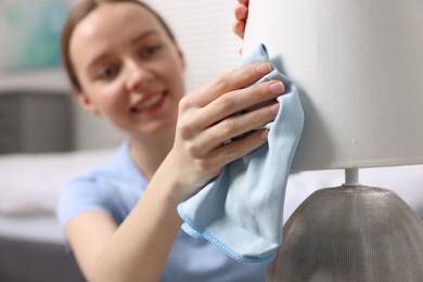 Photo of Woman with microfiber cloth cleaning lamp in bedroom, selective focus