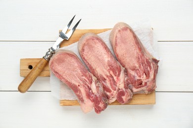 Photo of Raw beef tongue pieces and carving fork on white wooden table, top view