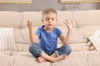Photo of Little boy meditating on soft sofa at home