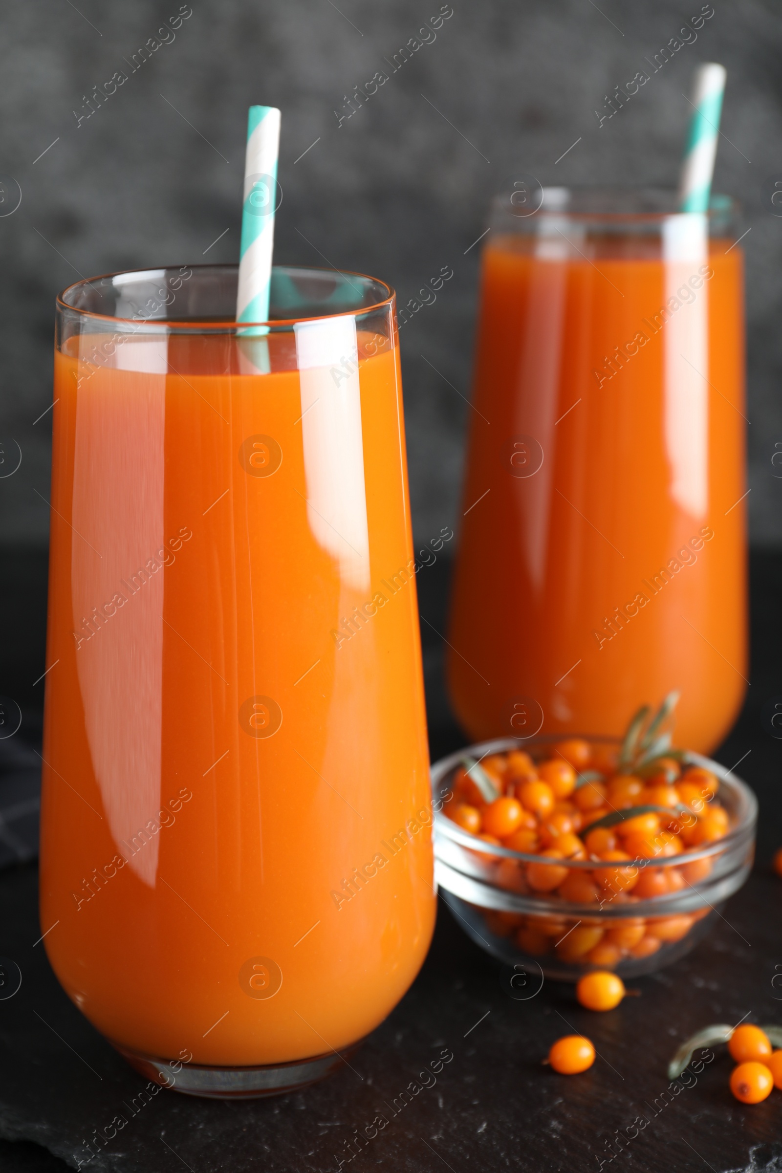 Photo of Delicious sea buckthorn juice and fresh berries on black table, closeup