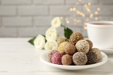 Photo of Delicious vegan candy balls on white wooden table against blurred lights, space for text