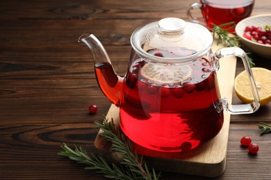 Photo of Tasty hot cranberry tea in teapot, rosemary and fresh berries on wooden table