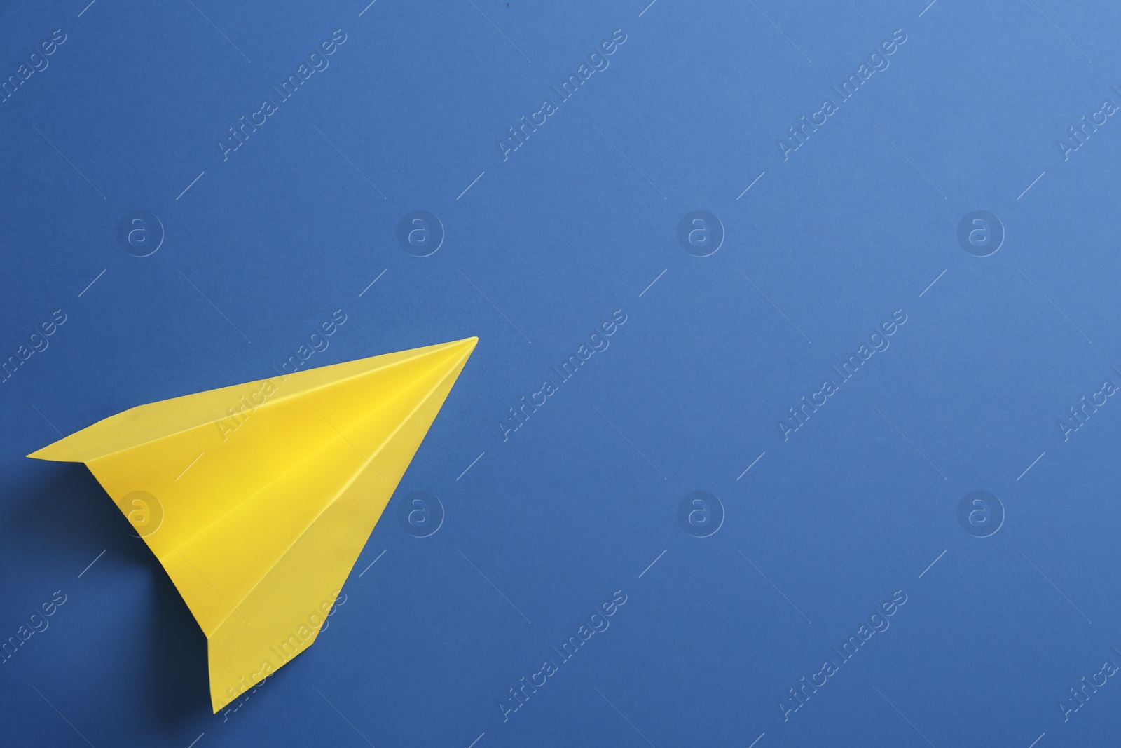 Photo of Yellow paper plane on blue background, top view. Space for text