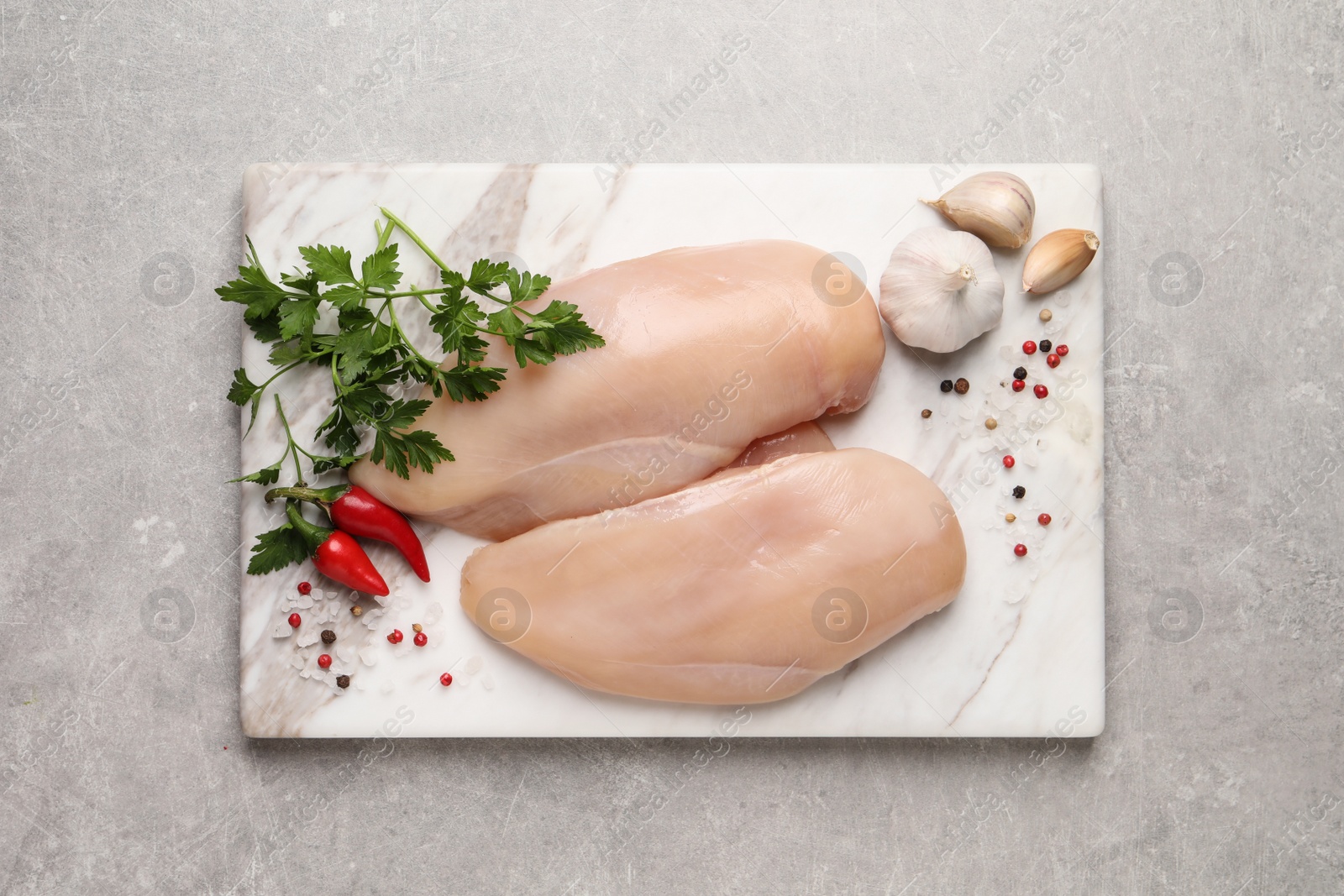 Photo of Raw chicken breasts and ingredients on light grey table, top view
