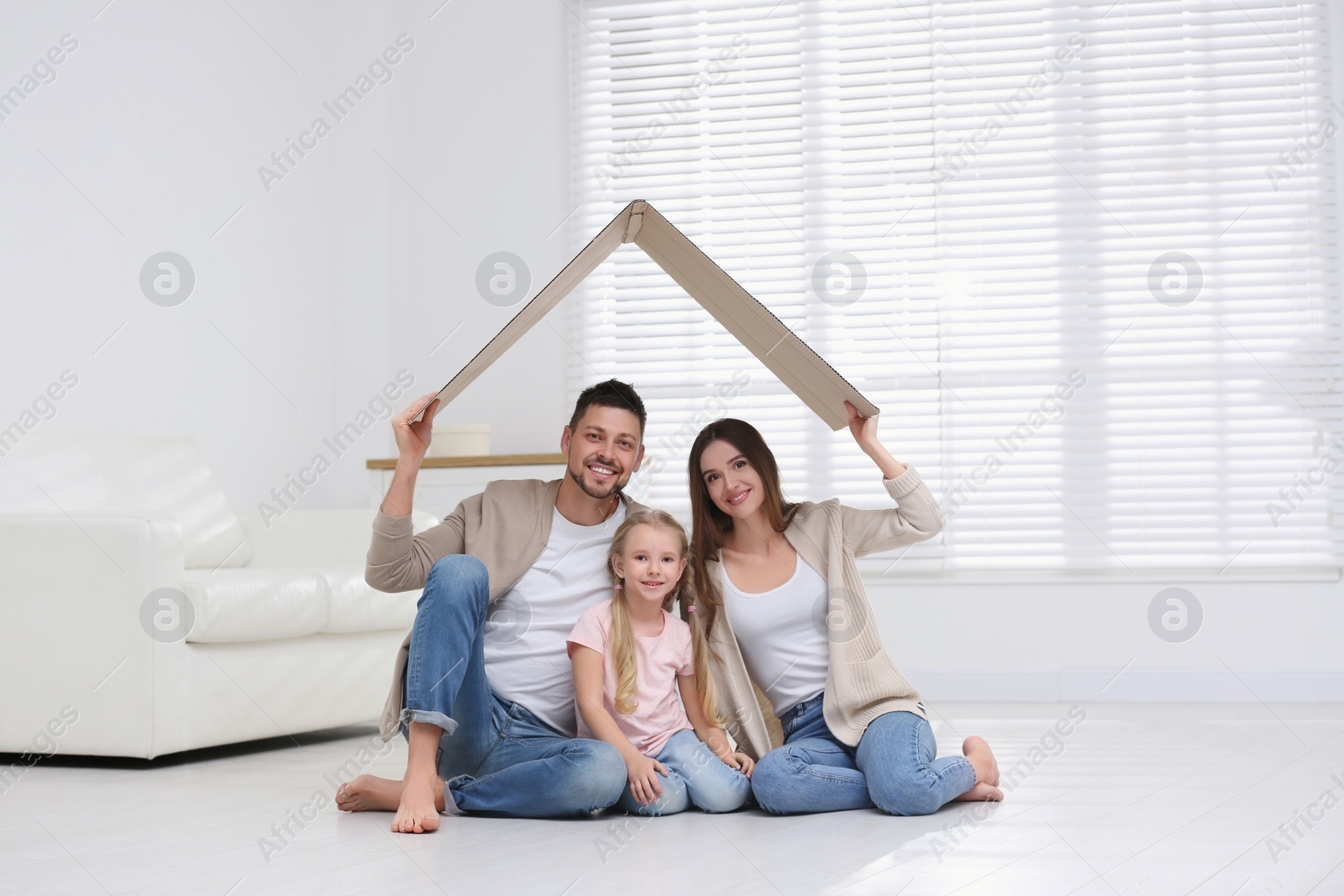 Photo of Happy family sitting under cardboard roof at home. Insurance concept