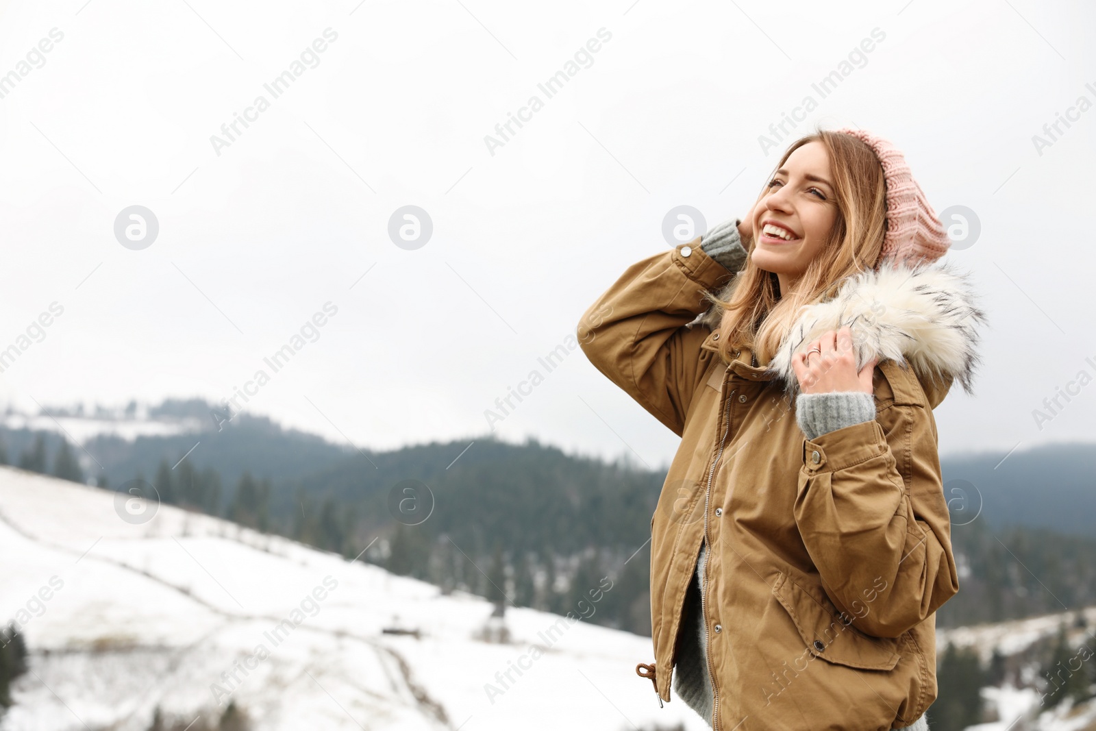 Photo of Young woman in warm clothes near snowy hill, space for text. Winter vacation