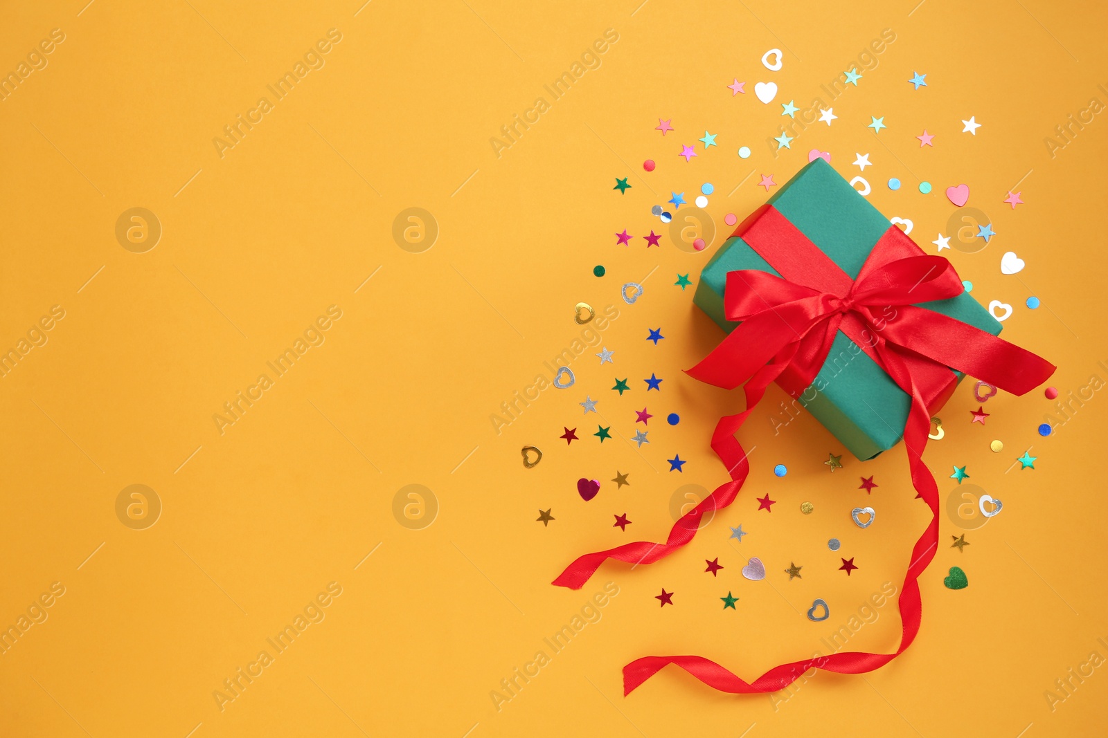 Photo of Gift box with sequins on orange background, flat lay. Space for text