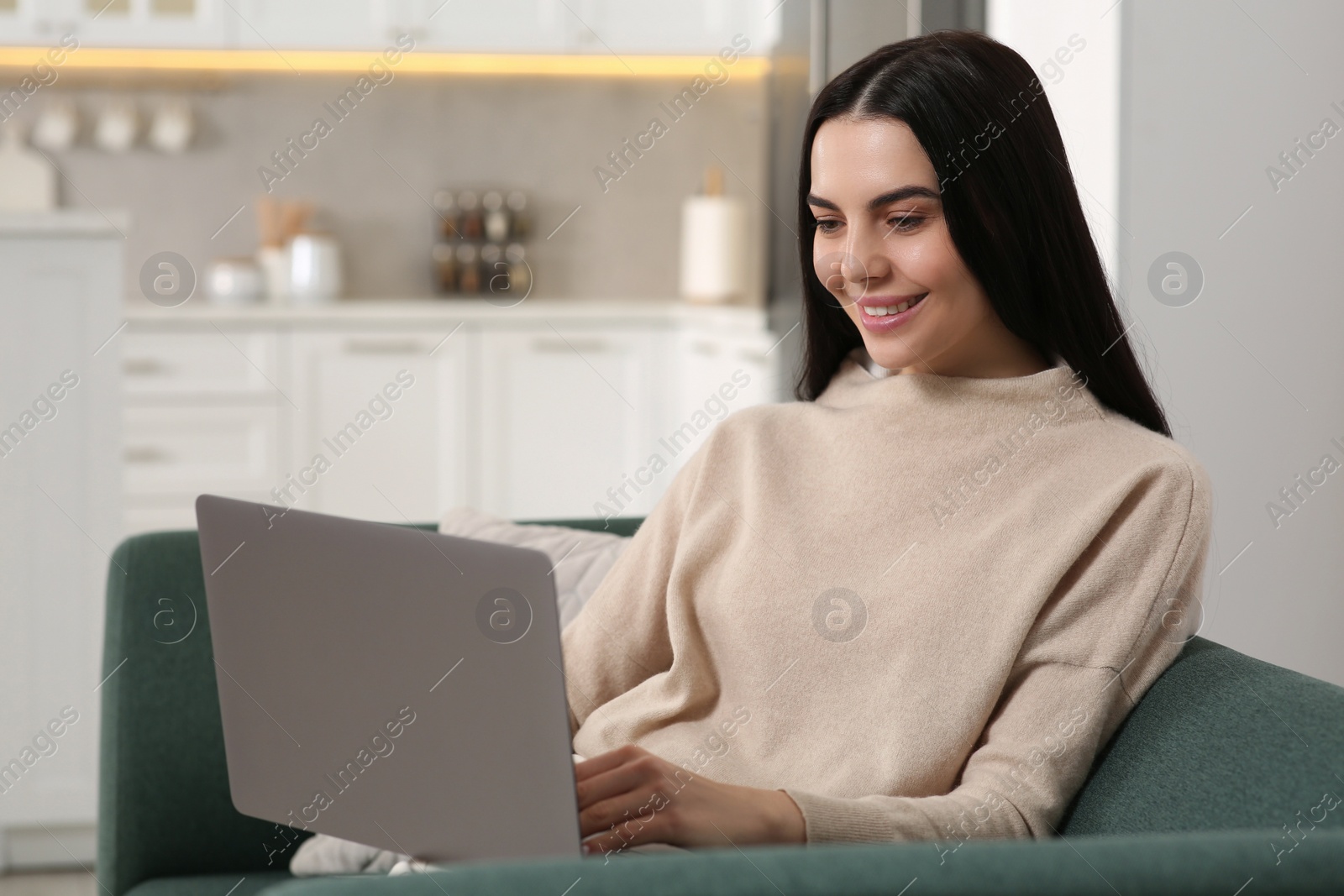 Photo of Happy woman working with laptop on sofa in kitchen