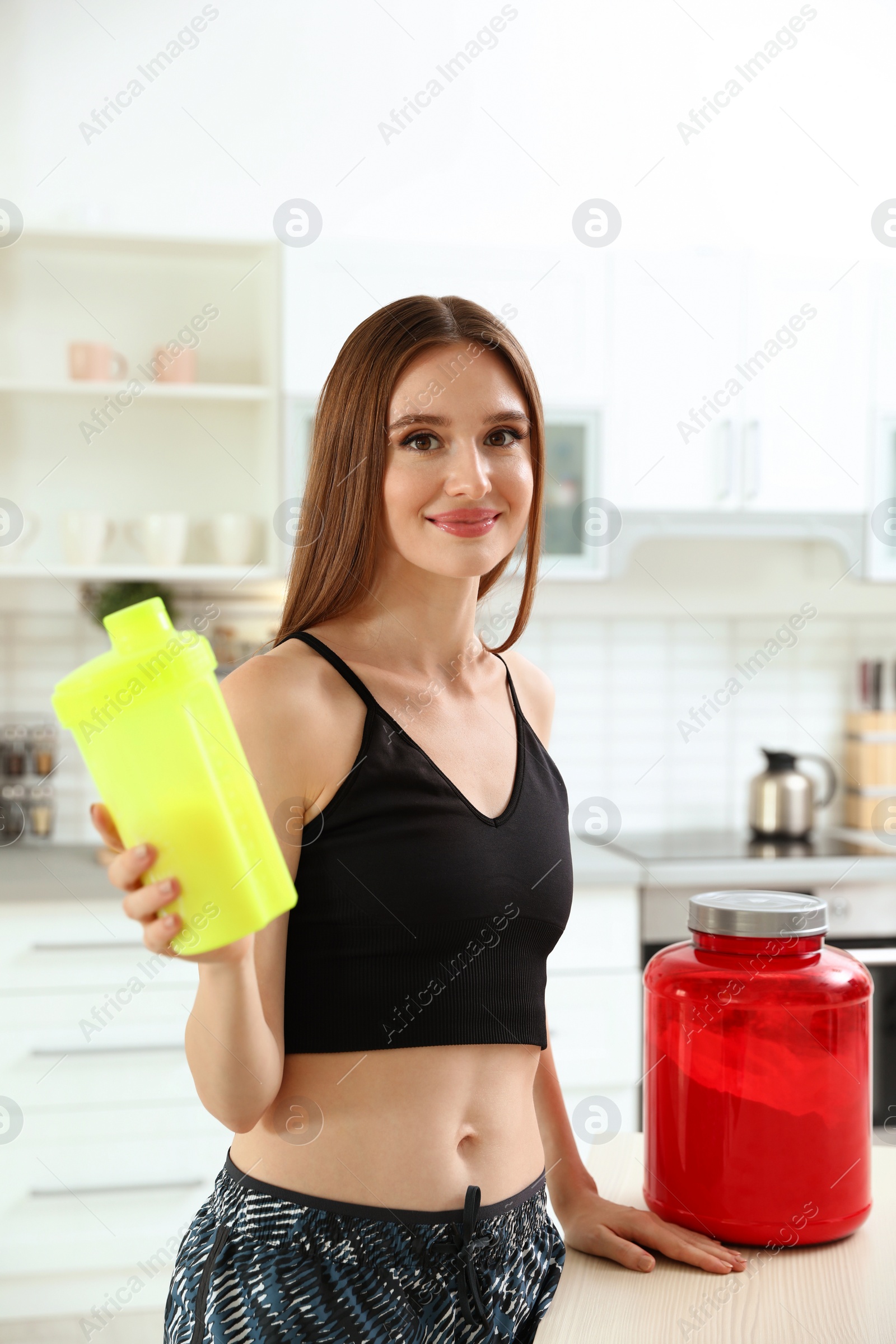 Photo of Young woman with bottle of protein shake in kitchen