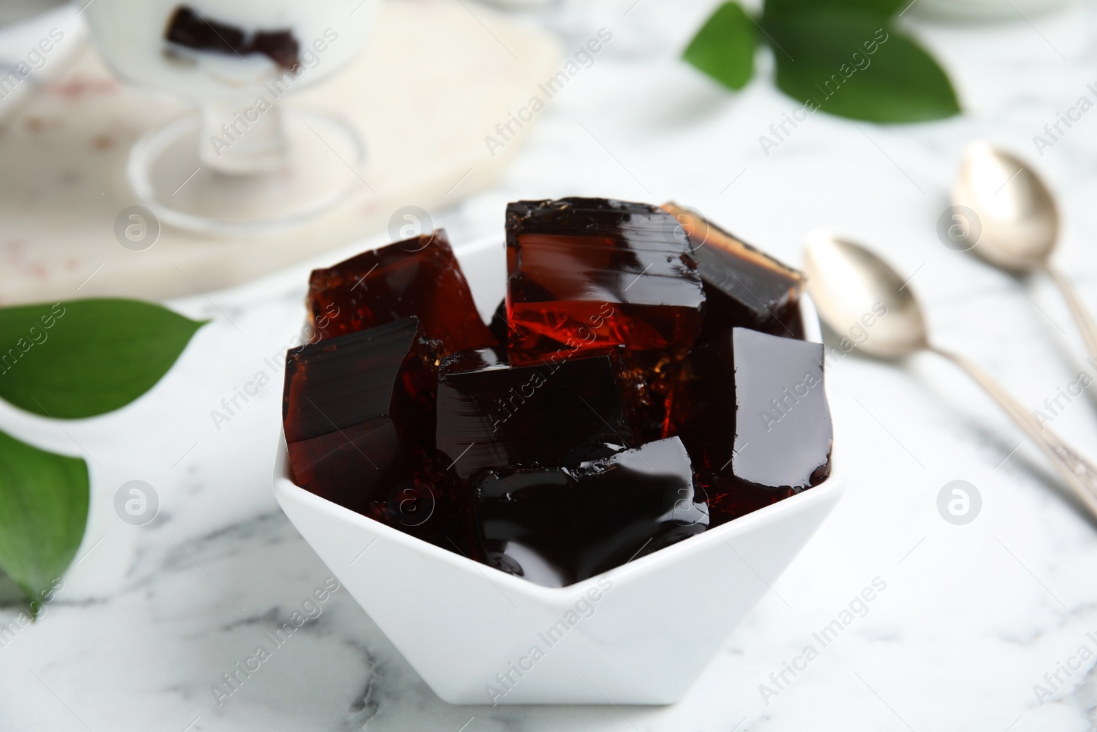 Photo of Delicious grass jelly cubes on white marble table, closeup