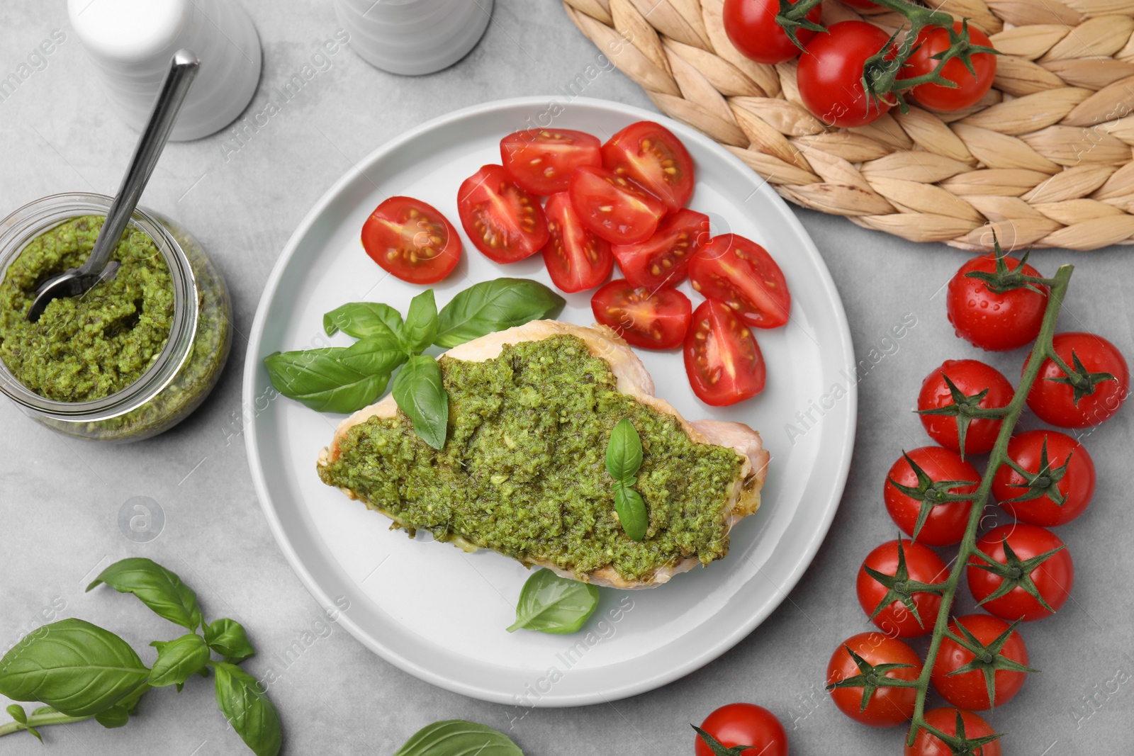 Photo of Delicious chicken breast with pesto sauce and tomatoes on light gray table, flat lay