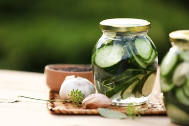 Photo of Jar of delicious pickled cucumbers and ingredients on wooden table against blurred background, closeup. Space for text