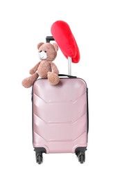 Photo of Red travel pillow and toy bear on suitcase against white background