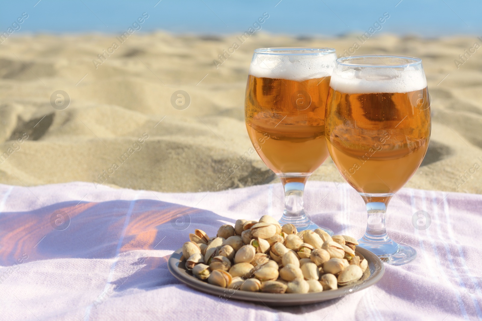 Photo of Glasses of cold beer and pistachios on sandy beach, space for text