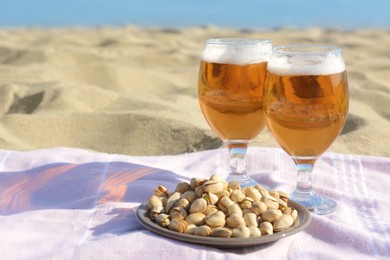Photo of Glasses of cold beer and pistachios on sandy beach, space for text