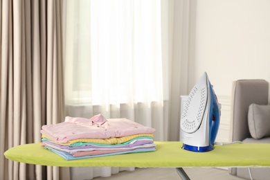 Photo of Board with modern iron and clean laundry at home