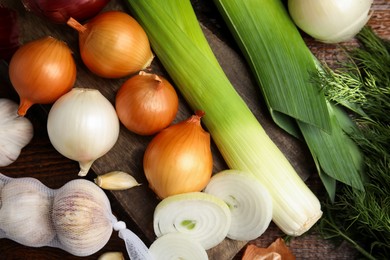 Fresh onion bulbs, leeks, garlic on wooden table, flat lay